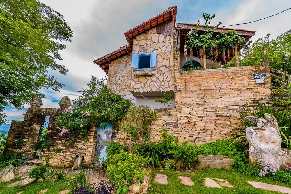 Jardim dos Anjos: muros de pedra, flores, folhagens e escultura de anjo diante do casarão